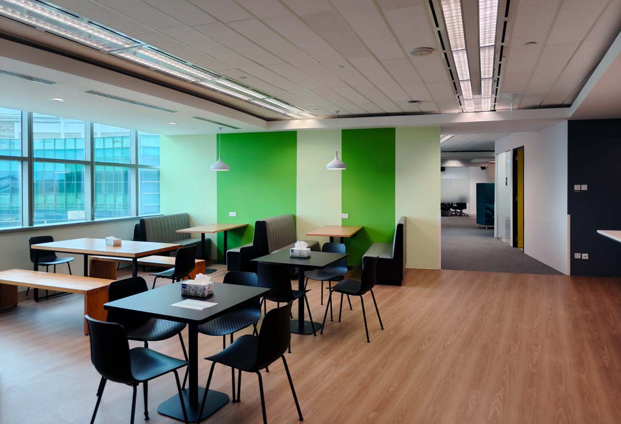 Tables and booth seating beside windows and a green feature wall. The Signature, AkzoNobel office.