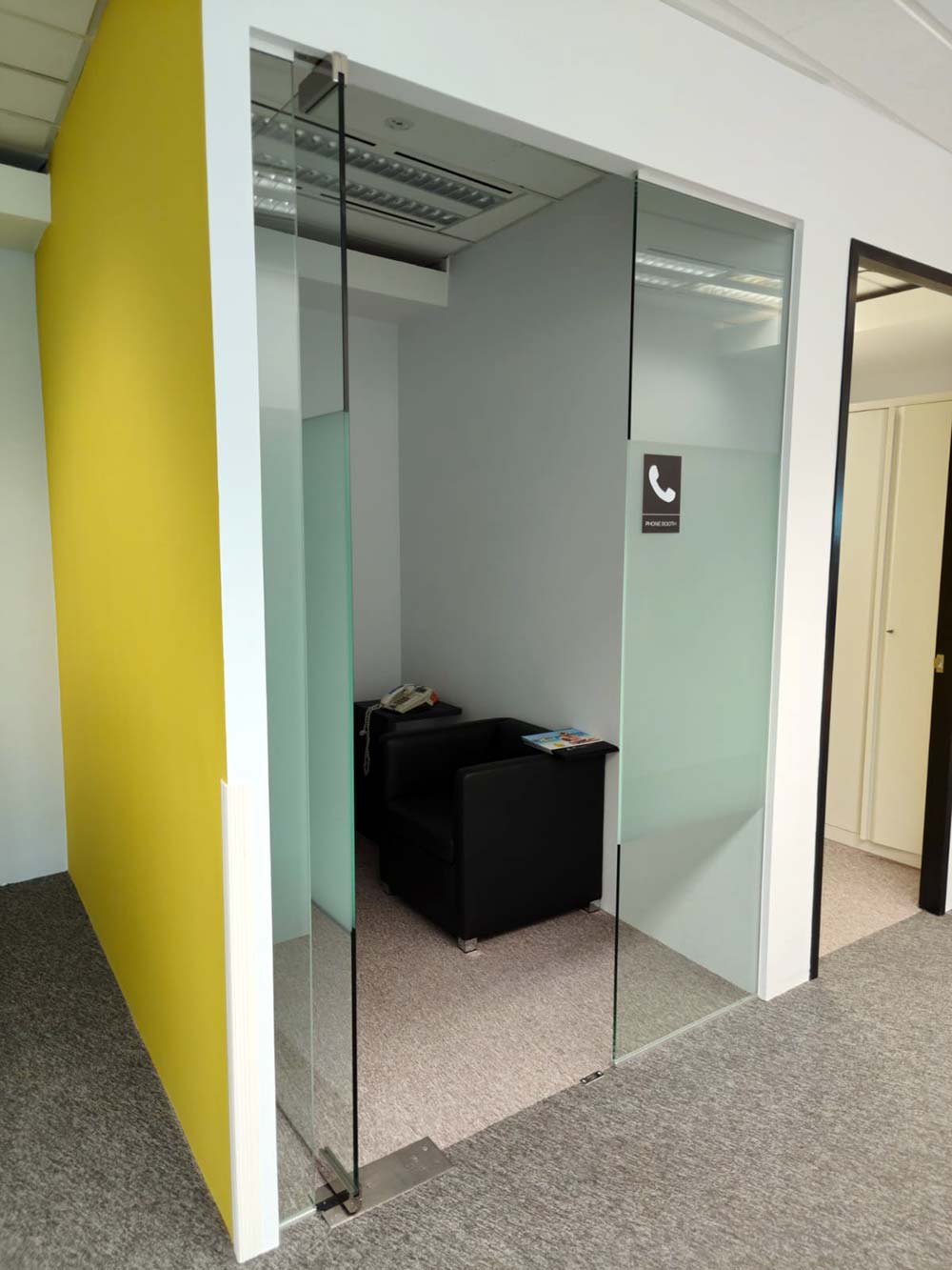 Glass-fronted phone room beside a yellow feature wall. The Signature, AkzoNobel office.